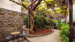 A garden with a stone wall, a gravel path, and a table with chairs. - Il Roseto (Ravello)