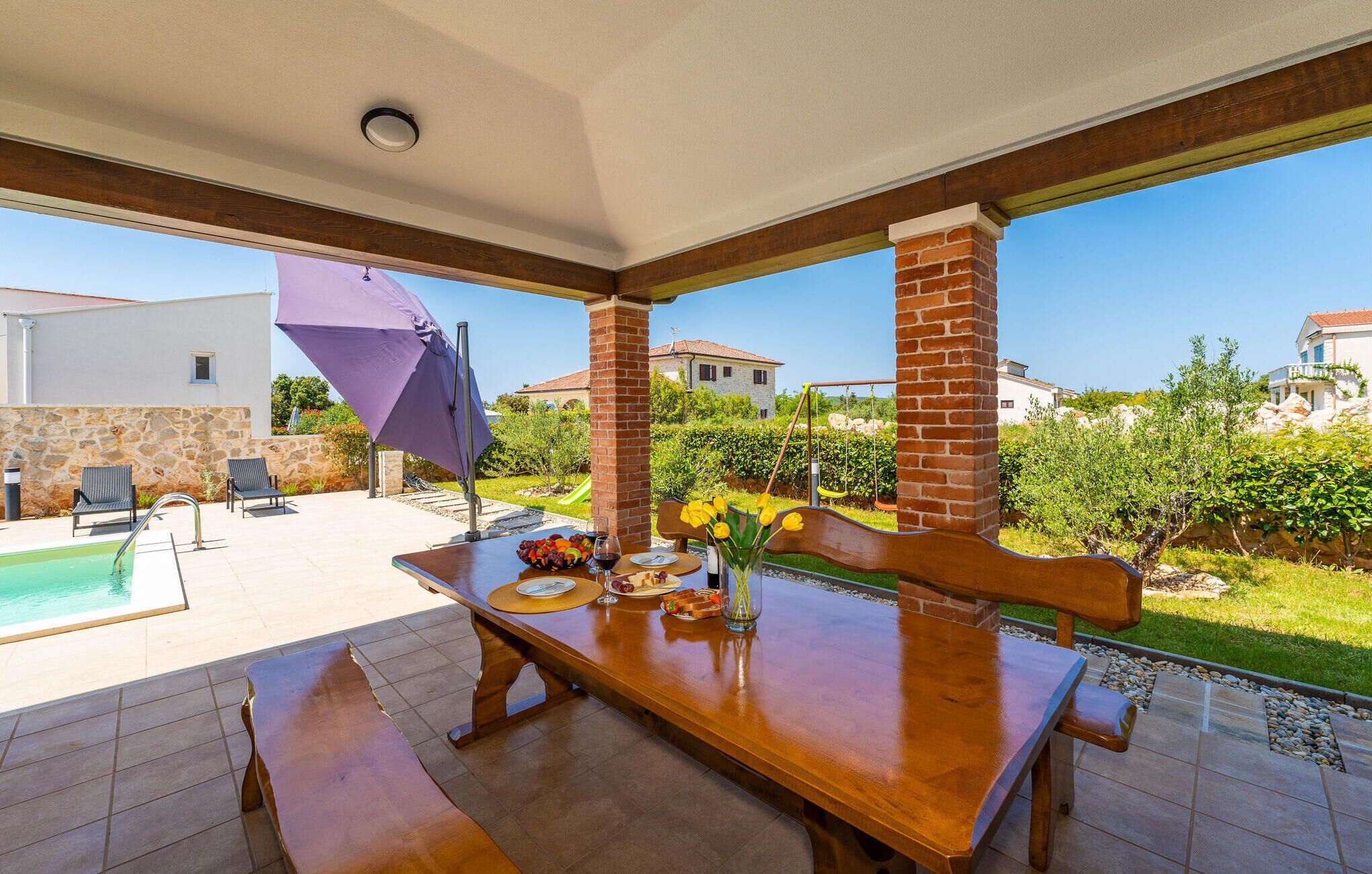 Un espace extérieur aménagé pour les repas, avec une piscine, un mur en pierre et une vue sur des maisons et de la verdure.