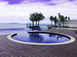 Ein kreisförmiger Infinity-Pool mit Holzterrasse, Palmen und Meerblick.
