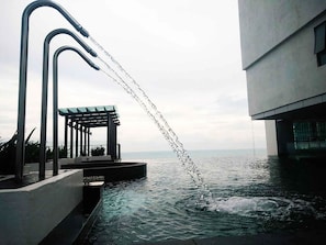 Uma piscina moderna ao ar livre com jatos de água, área de estar coberta e vista para o oceano.
