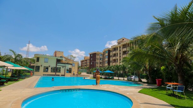 A swimming pool with a circular section, surrounded by palm trees and a building with balconies. - Suswa Six Apartment (Mombasa)