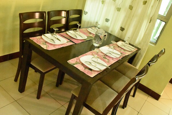 A dining table set with plates, cutlery, and a pitcher, surrounded by wooden chairs.