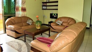 A living room with two brown leather sofas, a wooden coffee table, and a TV on the wall. - Suswa Six Apartment (Mombasa)
