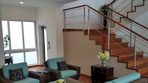 A living room with wicker furniture, a glass coffee table, and a staircase with wooden steps and metal railings. - La Maison 100 (Kuala Lumpur)