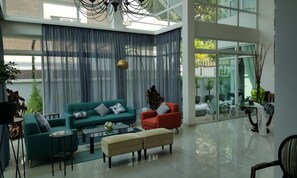 Un salón espacioso con un gran ventanal, un sofá verde, un sillón rojo y un otoman beige.