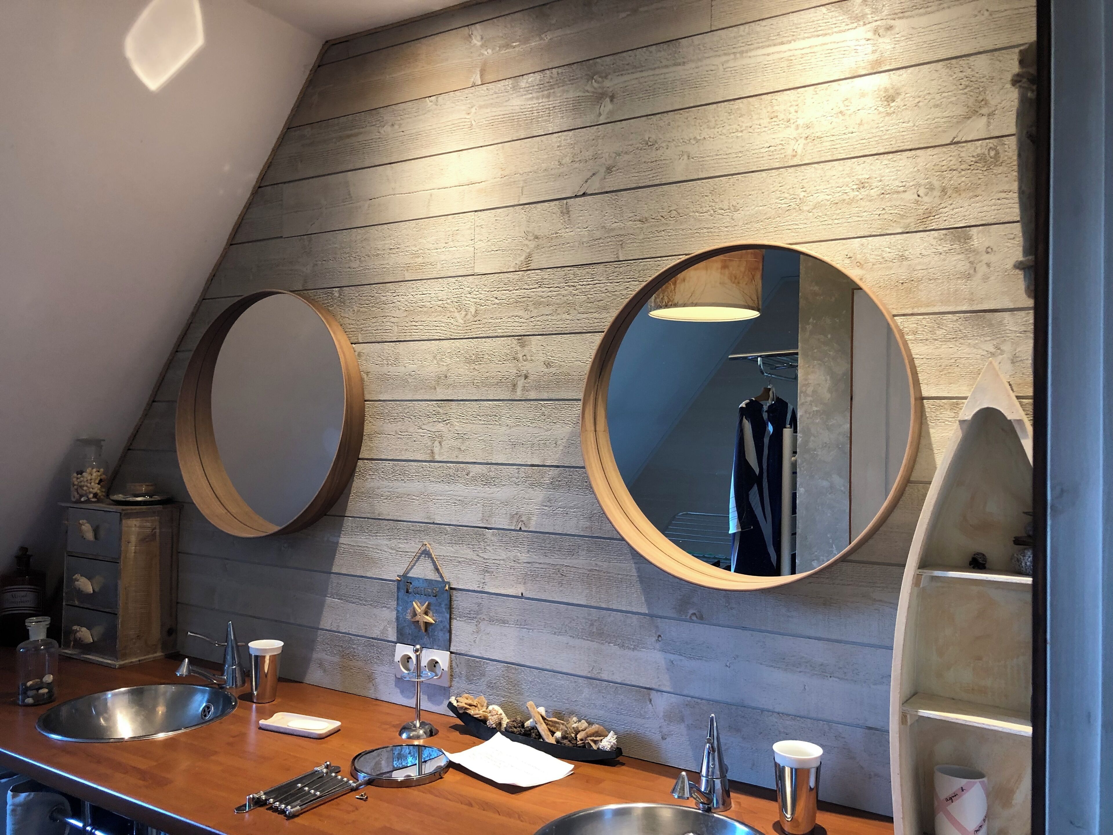 Une salle de bain moderne avec des murs recouverts de panneaux en bois, deux miroirs ronds, un lavabo et un porte-serviettes.