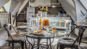 Un comedor con mesa de vidrio dispuesta para dos personas, con platos, vasos y una botella de jugo de naranja.