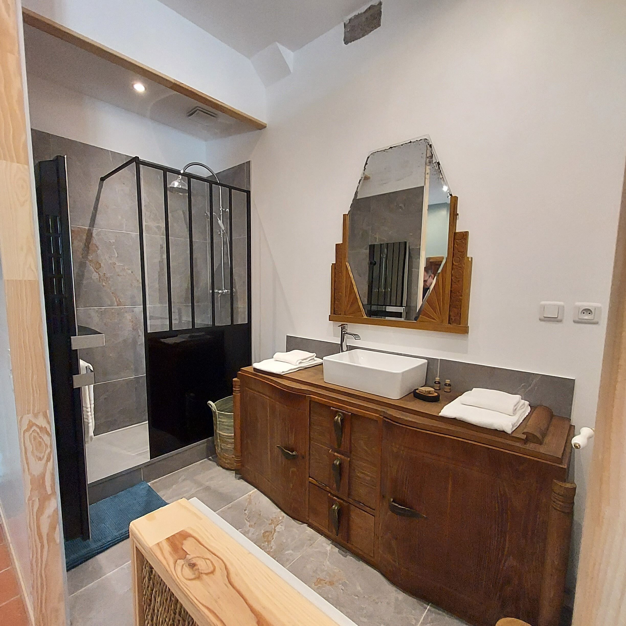 Un baño moderno con cabina de ducha, un espejo grande y un tocador de madera con lavabo.