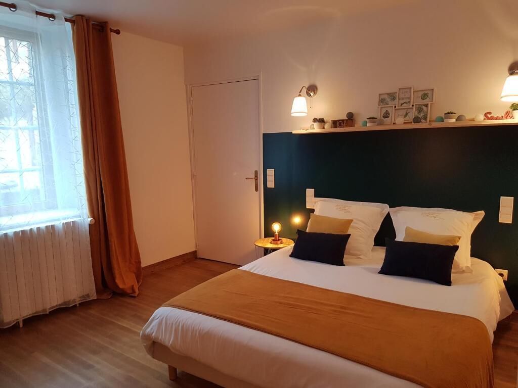 A hotel room with a large bed, a nightstand with a lamp, a window with curtains, and a wall with framed pictures.