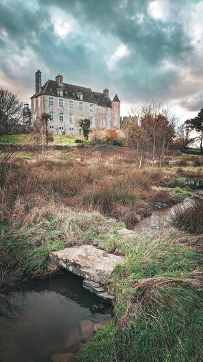 A historic stone building with multiple chimneys, a moat, and a small bridge. -  Le château du Rozel (Le Rozel)