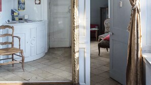 Um quarto com um espelho grande e trabalhado, um lustre e uma cadeira de madeira.