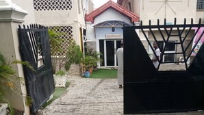 Ein gepflasterter Weg führt zu einem verschlossenen Eingang, im Hintergrund ein Gebäude.