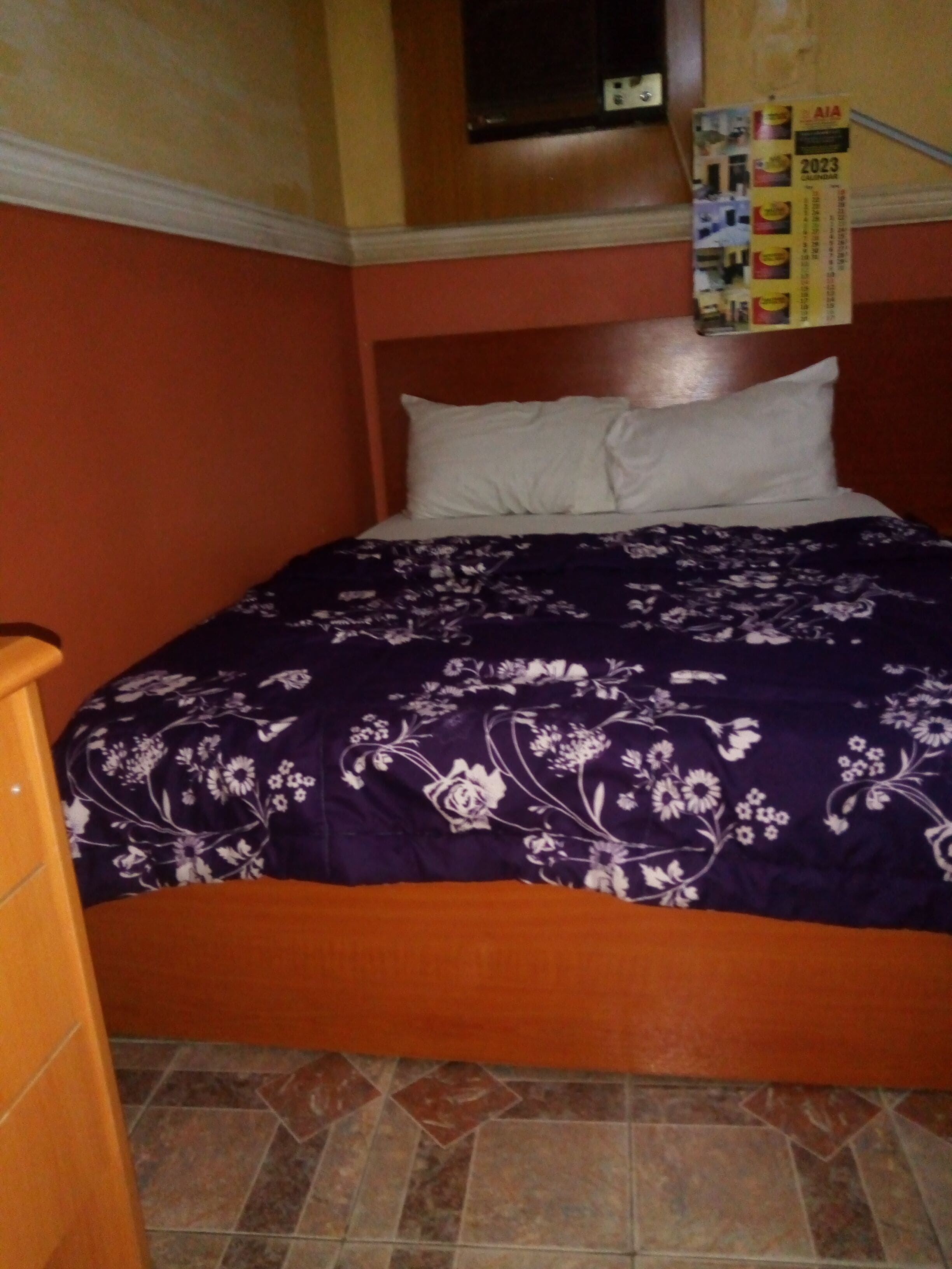 A bed with a floral-patterned bedspread, a wooden headboard, and a tiled floor.