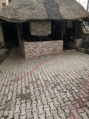 A thatched-roof structure with a zebra-patterned cushion, a brick wall, and a paved floor. - Maitama Guest House (Abuja)