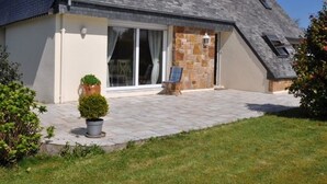 A house with a sloped roof, large glass sliding doors, a stone wall, and a paved patio. - House with enclosed garden for rent in Louannec, close to the sea (Louannec)