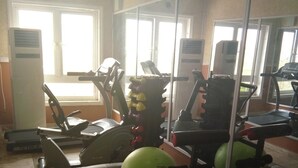 Ein Fitnessraum mit Trainingsgeräten, einem großen Spiegel und einer Uhr an der Wand.