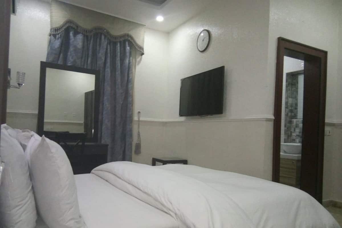 Ein Hotelzimmer mit einem Bett, einem an der Wand befestigten Fernseher, einer Uhr und einem Spiegel.