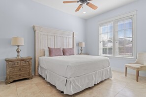 A bedroom with a large bed, wooden nightstands, a ceiling fan, and a window with blinds.