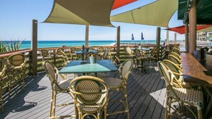 An outdoor dining area with wicker chairs and tables, overlooking the ocean.