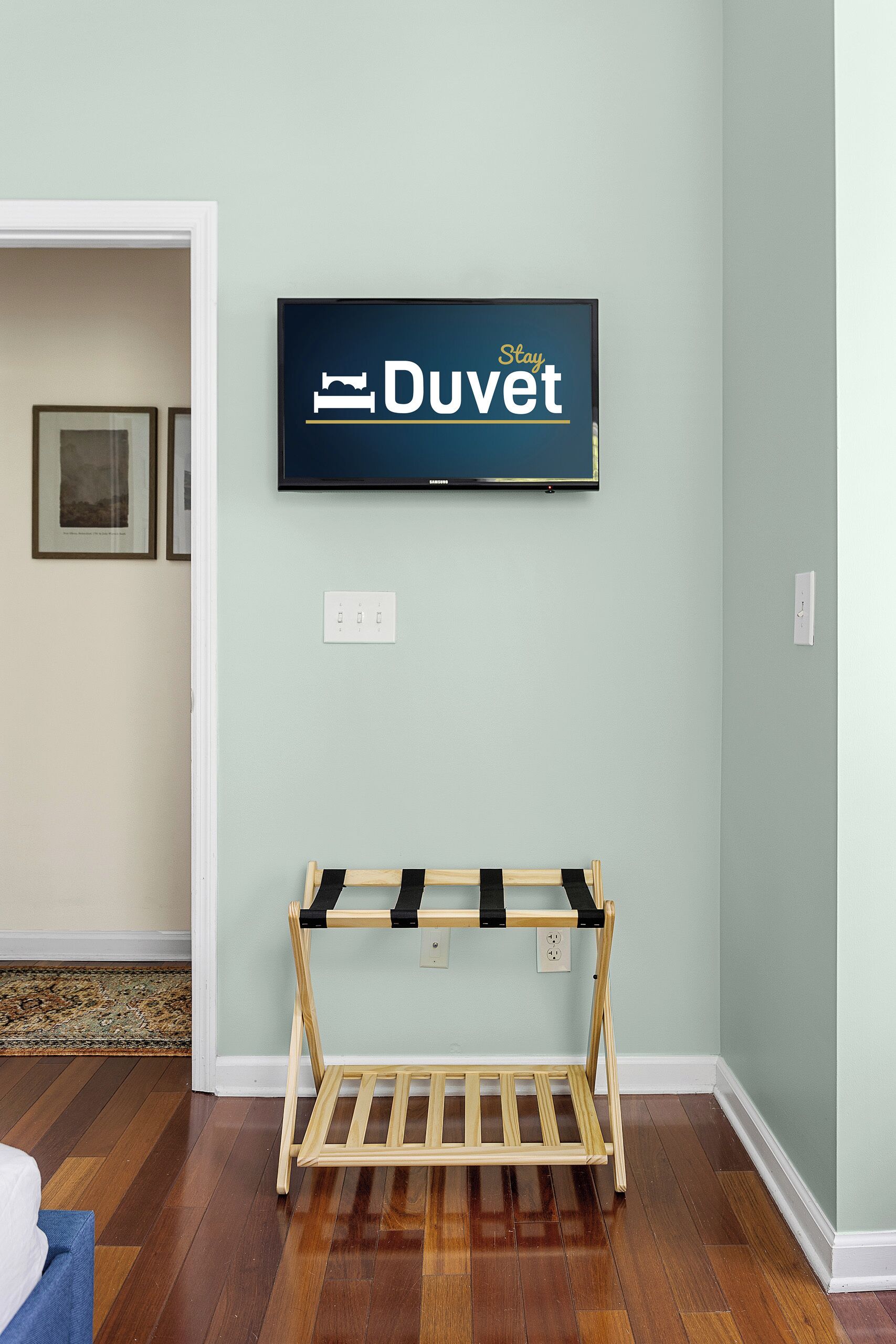 Ein Zimmer mit an der Wand montiertem Fernseher, der 'Duvet' anzeigt, einer Holzbank und Holzdielenboden.