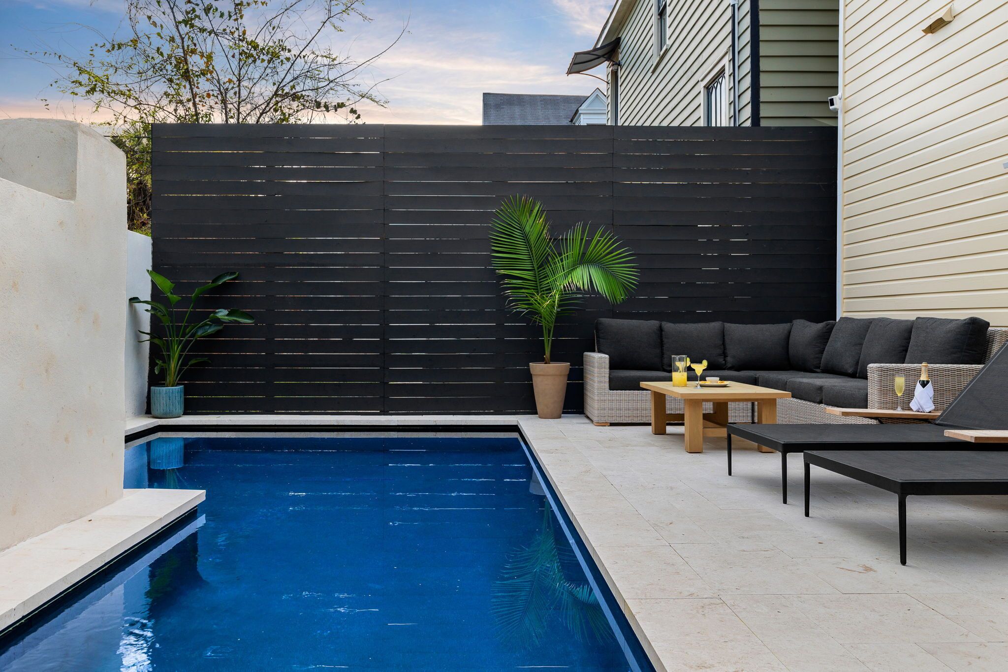 A modern outdoor pool area with a black fence, a sofa, and a table.