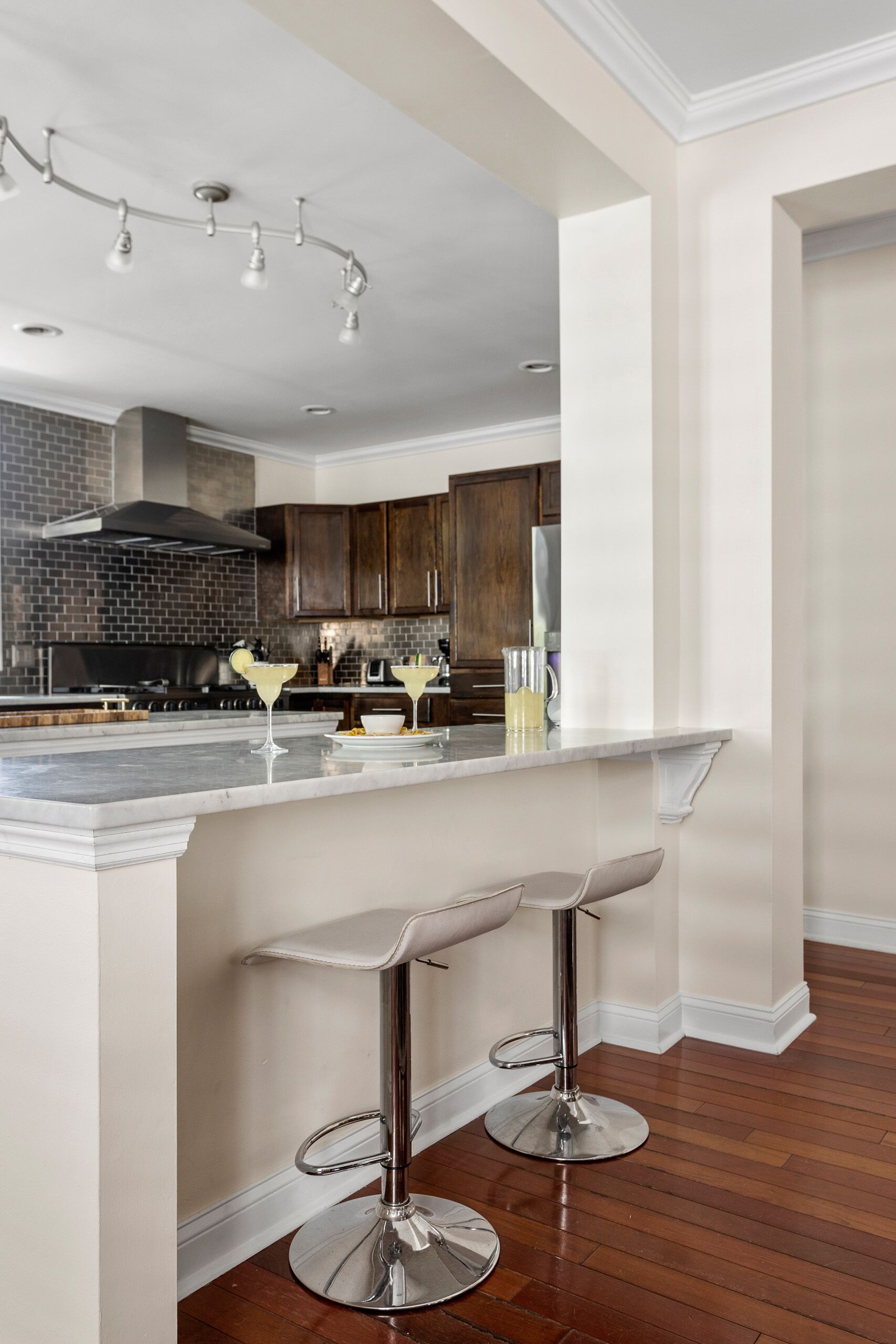 A modern kitchen with a marble island, two bar stools, and a brick backsplash.
