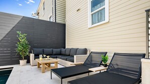 Eine Terrasse im Freien mit einer schwarzen Couch, zwei Lounge-Sesseln, einem Couchtisch und einem kleinen Pool.