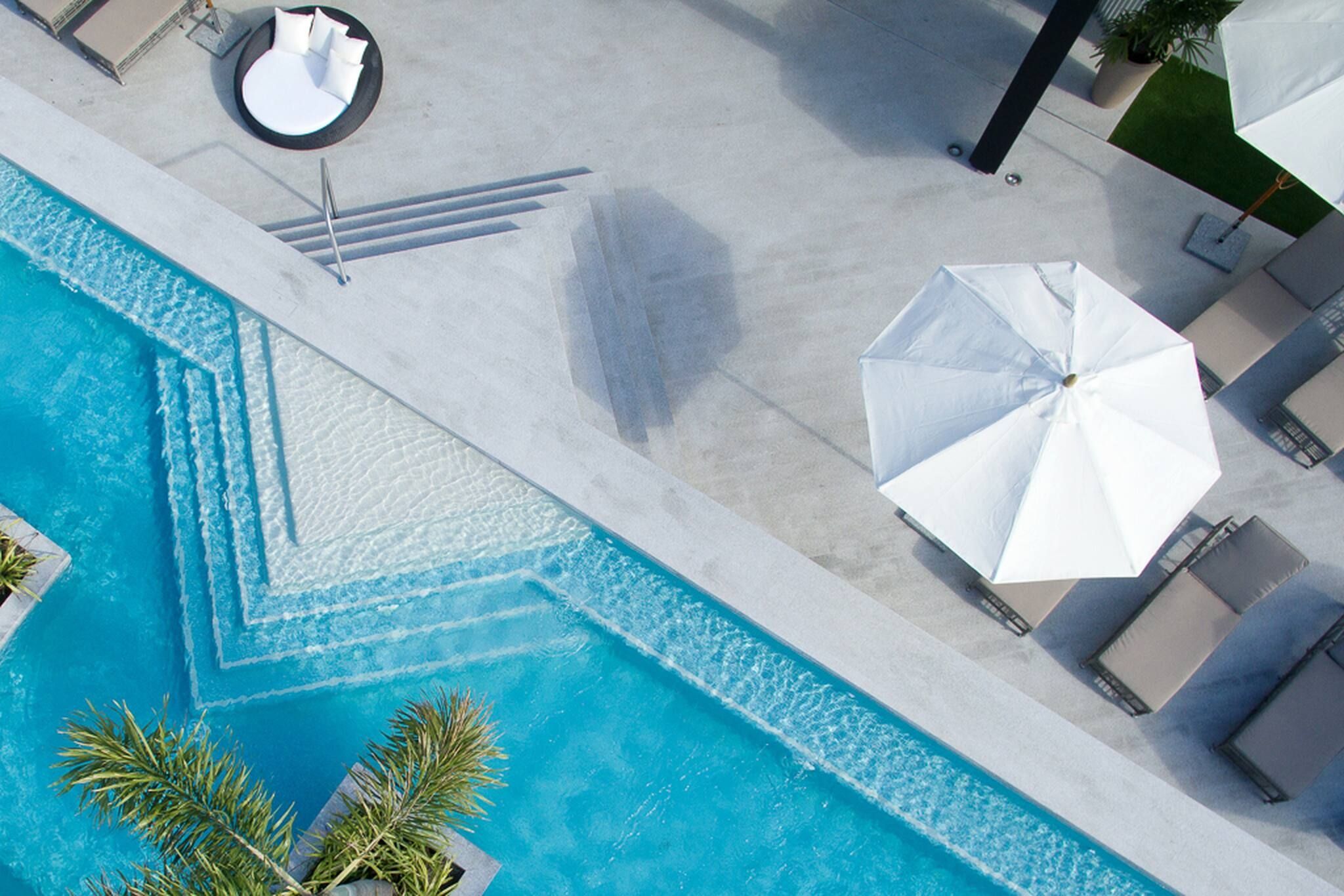 Vista aérea de una piscina con diseño geométrico, rodeada de sillas de descanso y sombrillas.