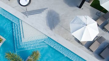 Eine Vogelperspektive zeigt einen Swimmingpool mit einem geometrischen Muster, umgeben von Liegestühlen und Sonnenschirmen.