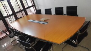 Un salón de conferencias con una gran mesa ovalada, sillas negras y una pizarra.
