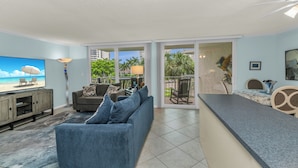 A living room with a TV, sofa, and a balcony with outdoor furniture. - 1 Bedroom / New Furniture / Direct beach access / Across from J.W. Marriott! (Marco Island)