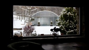 A window with a view of a snow-covered garden and a greenhouse. - Hotel Cruells (Planoles)