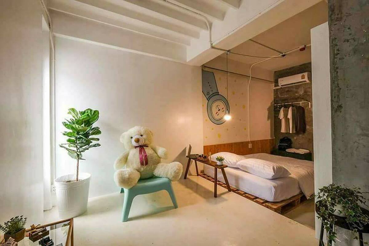 A small, cozy room with a bed, a chair, a potted plant, and a teddy bear.
