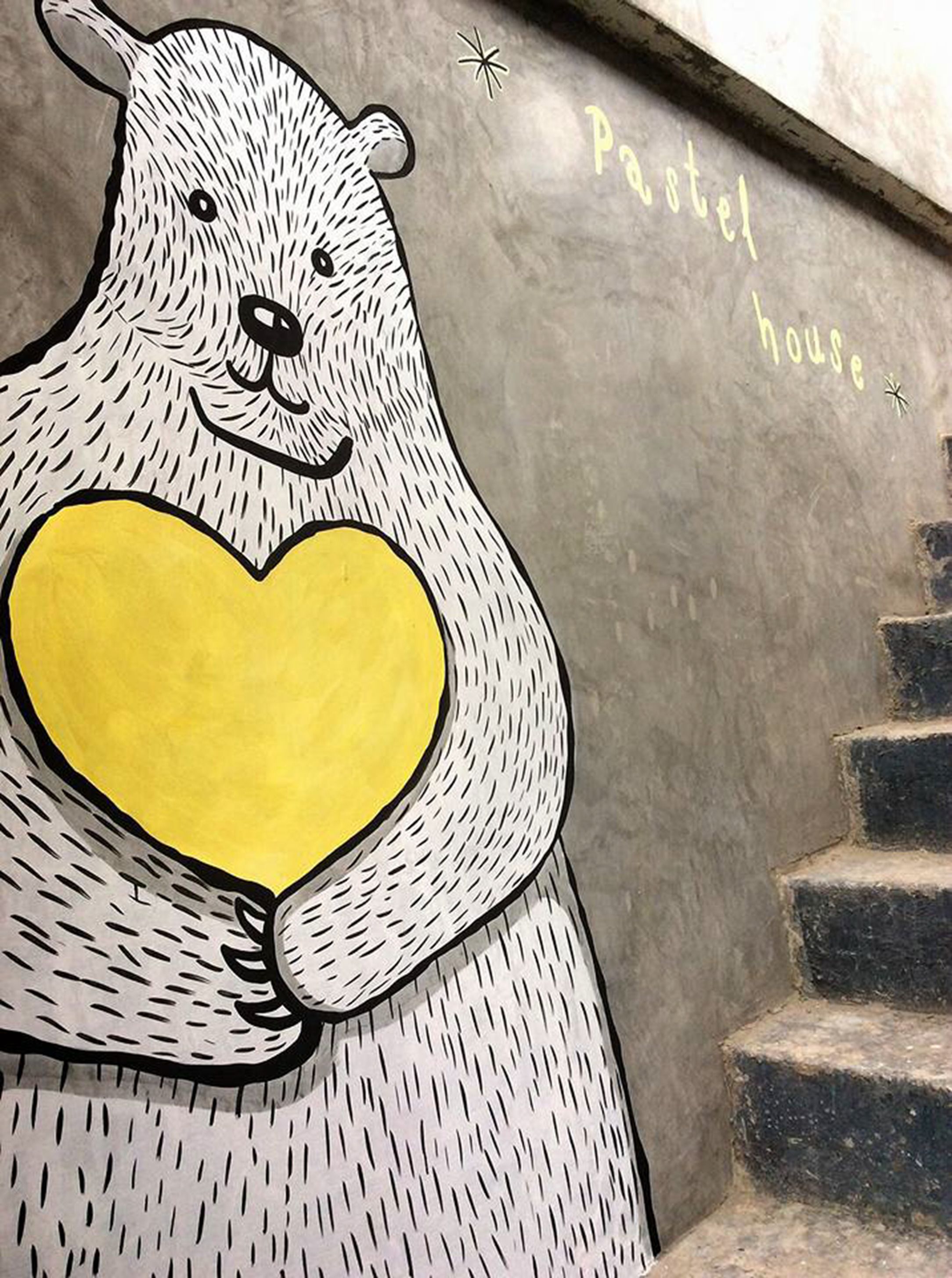Ein Bär hält ein Herz, auf der Wand steht "Pastel House" geschrieben.