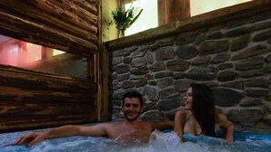 Una pareja en un jacuzzi con paredes de piedra y vigas de madera.