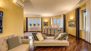 A living room with a beige sofa, patterned pillows, and a view of the city through large windows.