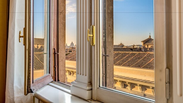 A window with a view of a historic building with classical architecture and a clear sky.