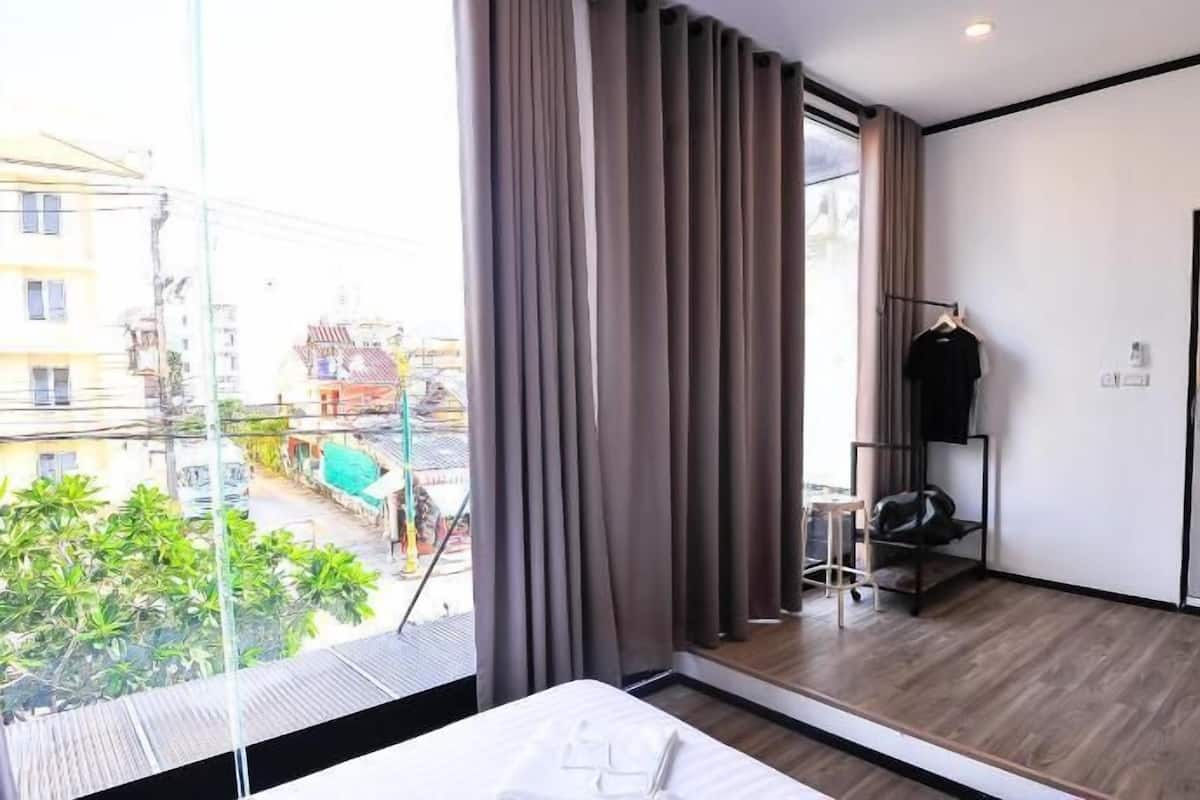 Una habitación de hotel moderna con un ventanal grande, una cama, un armario y una pequeña zona de estar.
