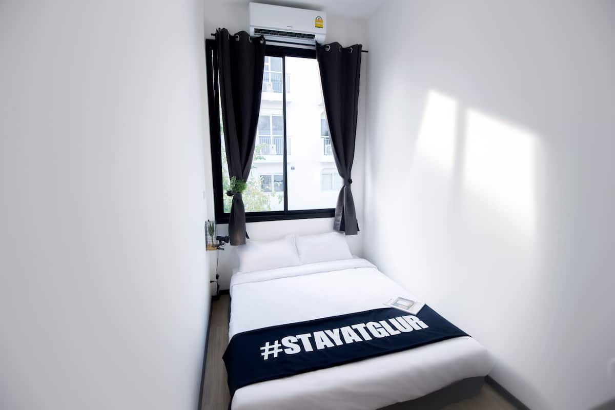 Una habitación de hotel pequeña con una cama, una ventana con cortinas y un aire acondicionado instalado en la pared.
