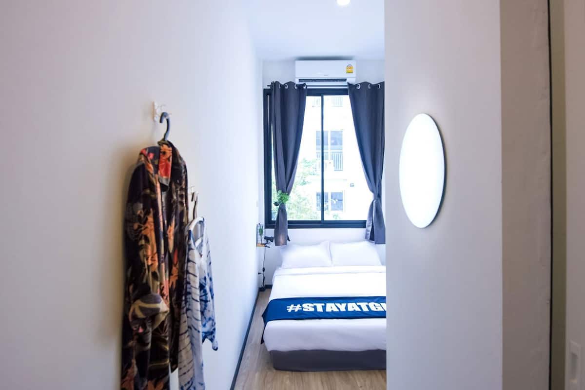 Habitación de hotel con cama, espejo adosado a la pared, ventana con cortinas y perchero con ropa.