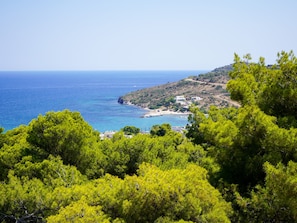 A coastal landscape with a clear view of the sea, a sandy beach, and a small settlement with buildings. - Pefkides Aegina Apartments (Aegina)