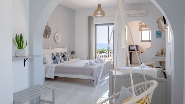 A modern bedroom with a bed, a hanging chair, and a balcony with a view. - Pefkides Aegina Apartments (Aegina)