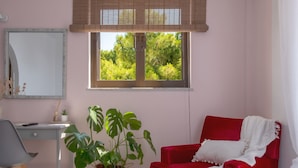 A room with a desk, chair, red sofa, large potted plant, window with blinds, and a mirror. - Pefkides Aegina Apartments (Aegina)