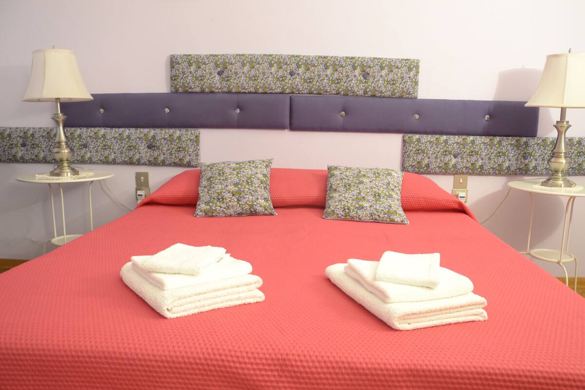 Un lit avec une couvre-lit rouge, deux oreillers et deux serviettes pliées.
