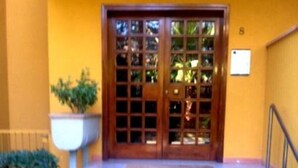 A building entrance with a wooden door, steps leading up to it, and a small planter with a plant to the left.