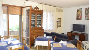 A dining area with tables set for four, a television, and a cabinet with glassware.