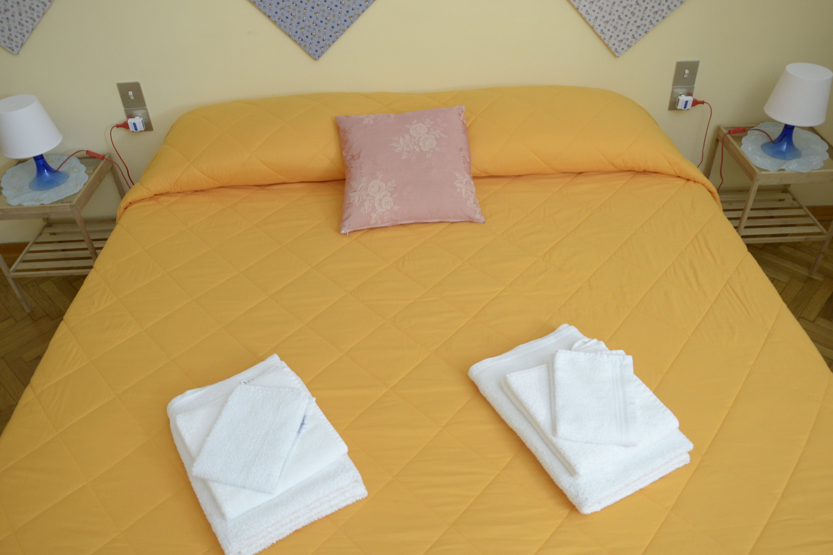 A bed with an orange bedspread, a pink pillow, and two folded white towels.
