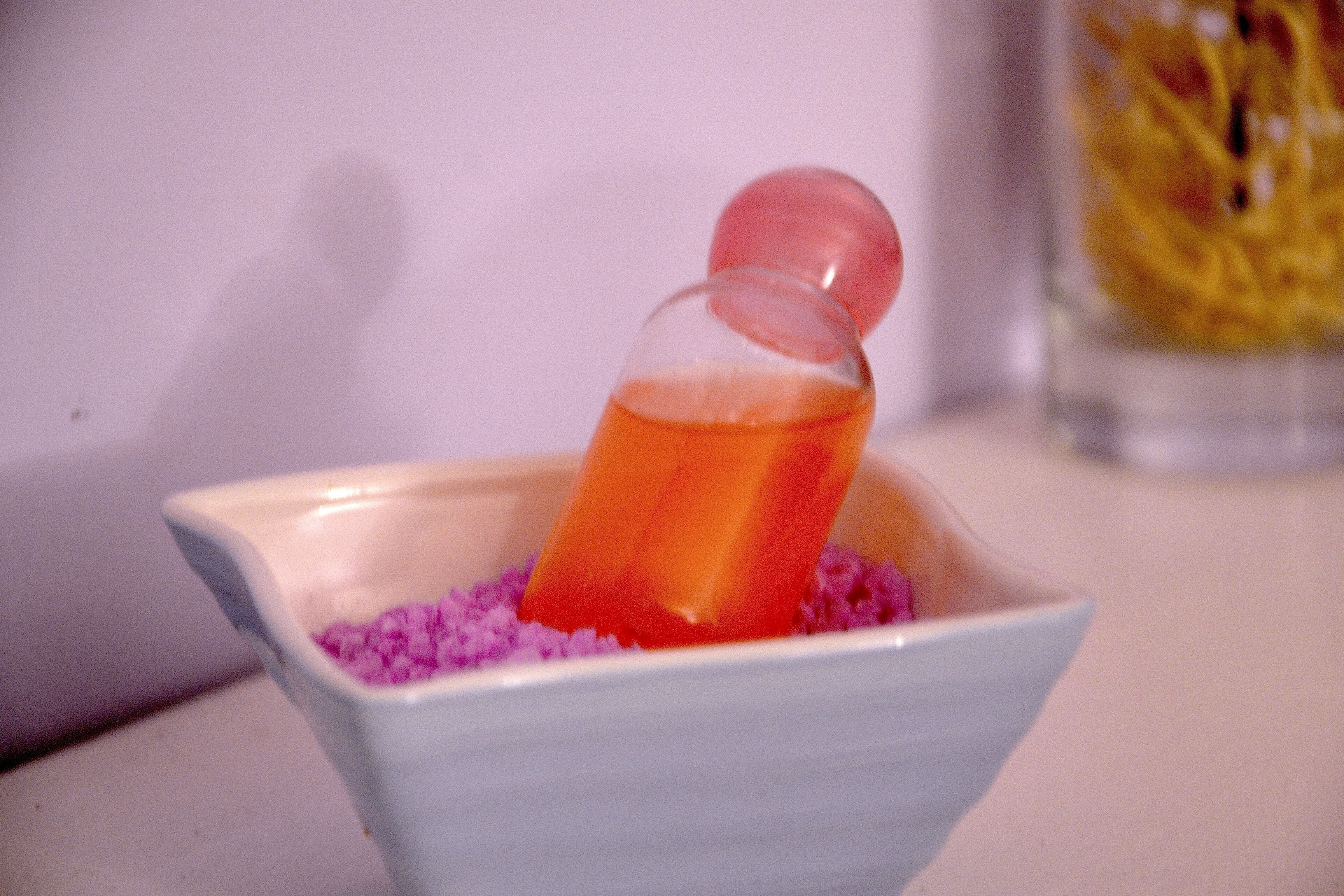 A small white bowl containing a clear liquid with a red object inside, set on a surface with a blurred background.