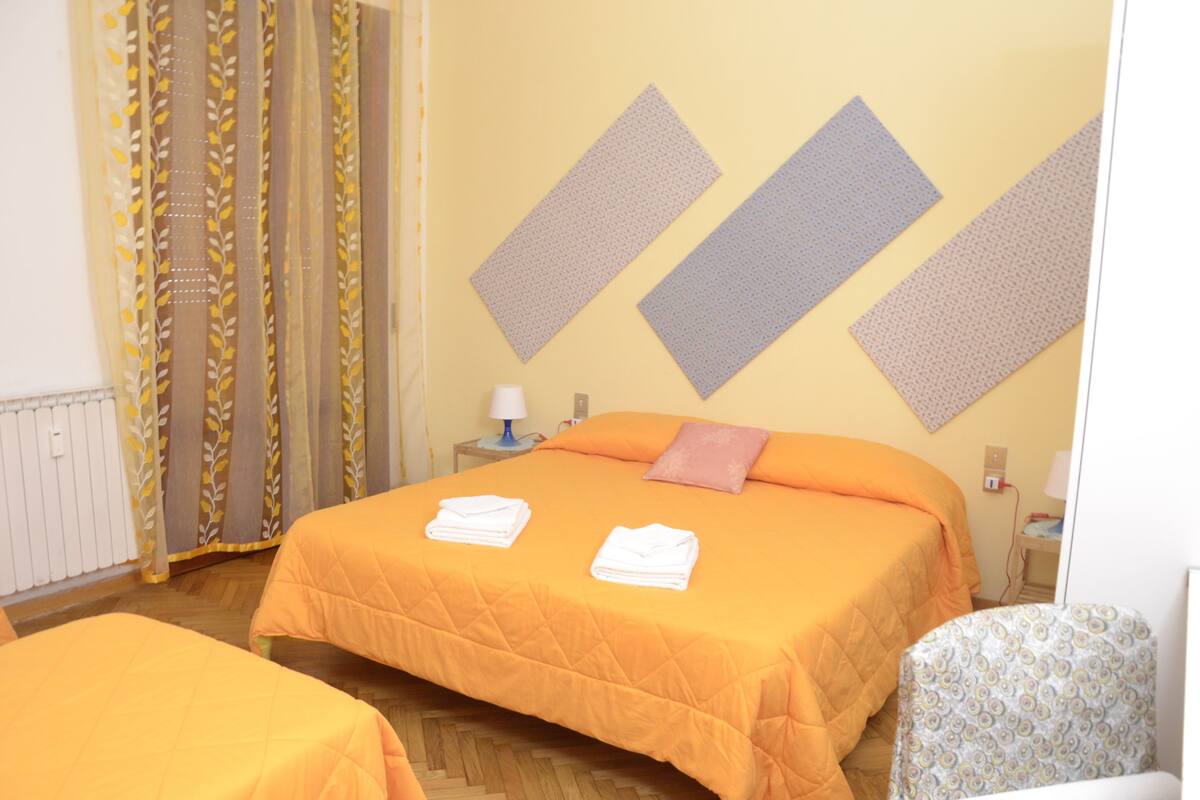 Une chambre d’hôtel avec deux lits, un rideau à motifs, une lampe fixée au mur et une petite table de chevet.