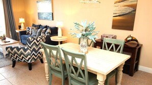 Un coin repas avec une table en bois et des chaises vertes, une petite table d’appoint avec une lampe et un vase décoratif contenant une plante.